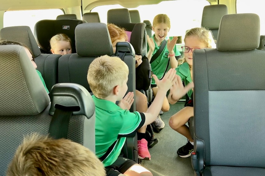 Several primary school children wearing green polo shirts riding on a school bus.