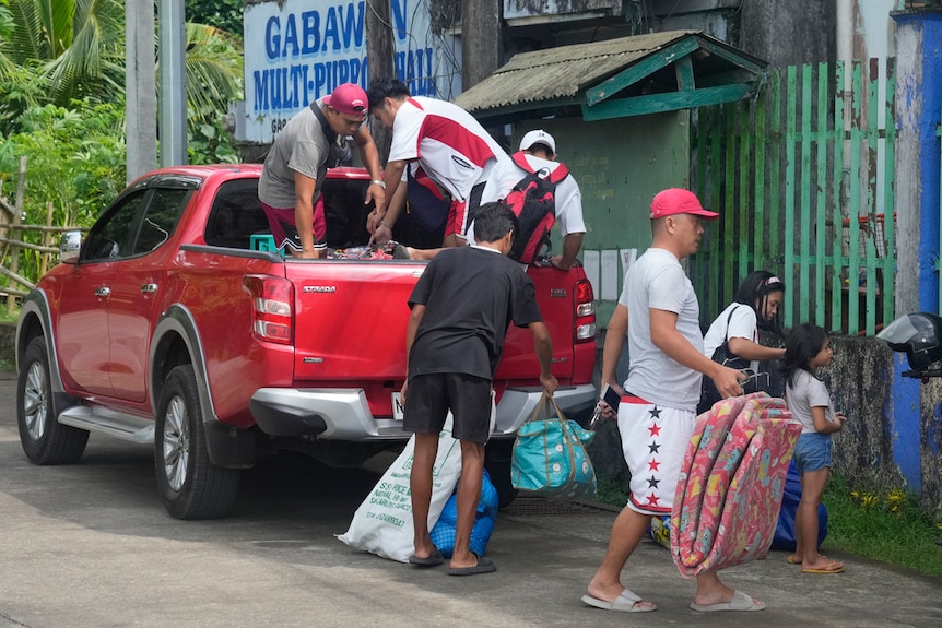 Evacuees carry their belongings as they arrive at a temporary relocation site at a school in Daraga town, Legaspi.