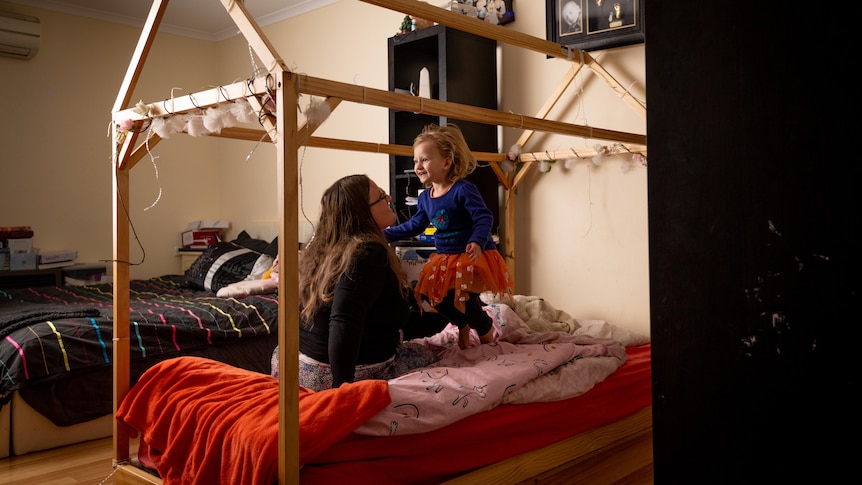 A woman holding a girl wearing a red tutu on a four poster bed
