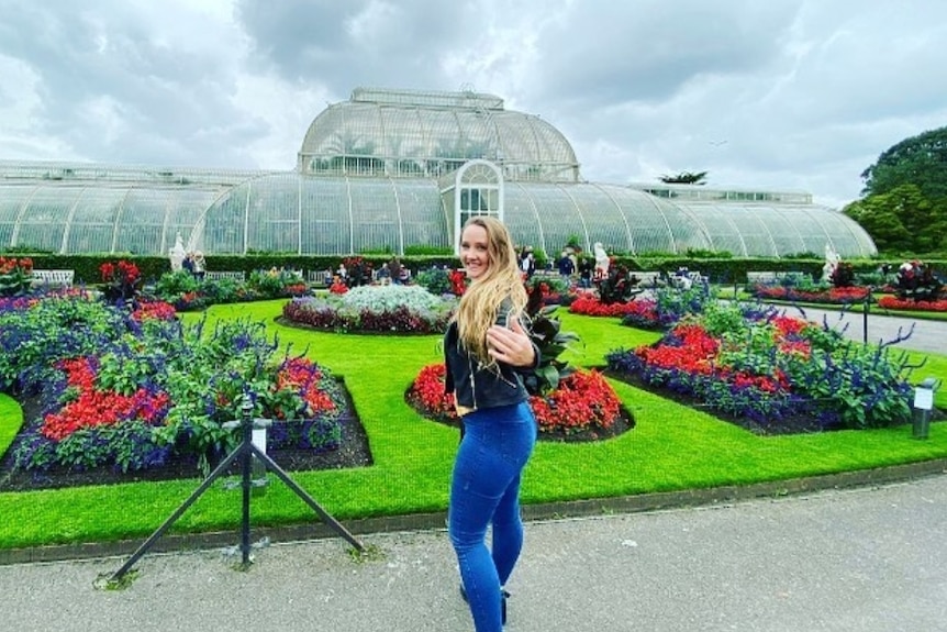 Woman wearing blue jeans smiles at camera in lush green garden