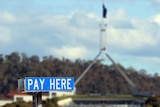 A sign says PAY HERE, with Canberra Parliament House visible in the background.