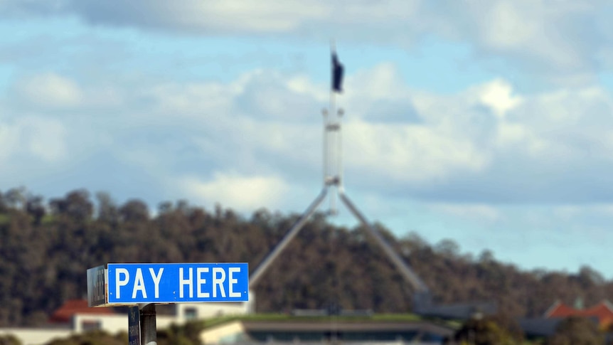 A sign for paid parking with Parliament House in the background.