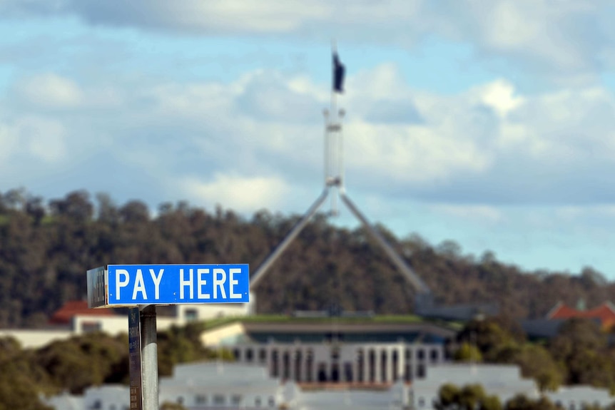 A sign for paid parking with Parliament House in the background.