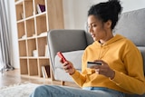 Woman shopping on her phone while holding a credit card at home