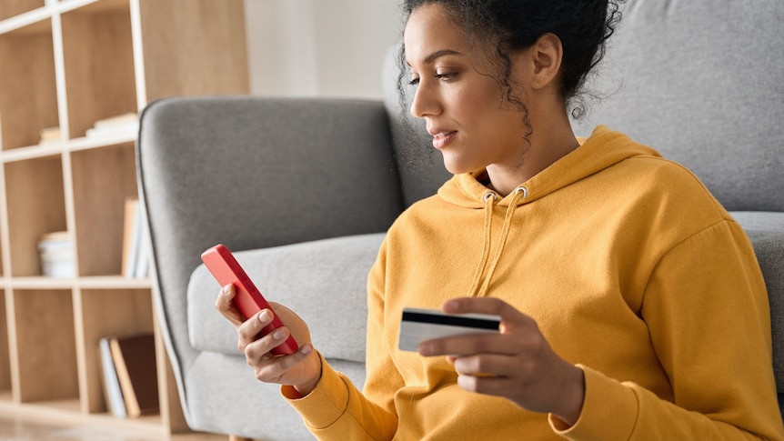 Woman shopping on her phone while holding a credit card at home