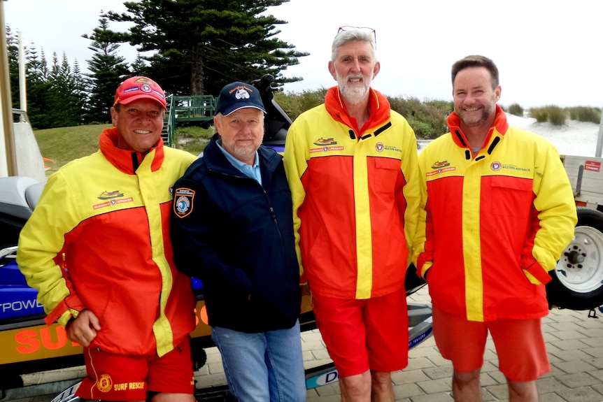 A group of sea rescue volunteers in high-viz clothing pose in front of a jetski at the beach.
