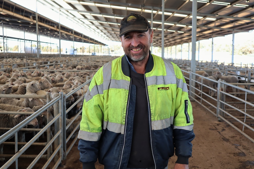 Man in yellow high vis jacket smiling, standing in sheep sale yard.
