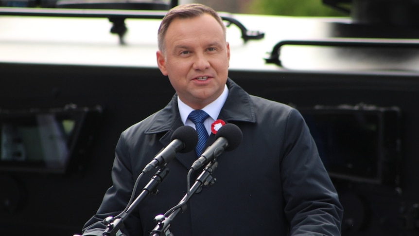 Polish President Andrzej Duda stands before a podium with microphones.