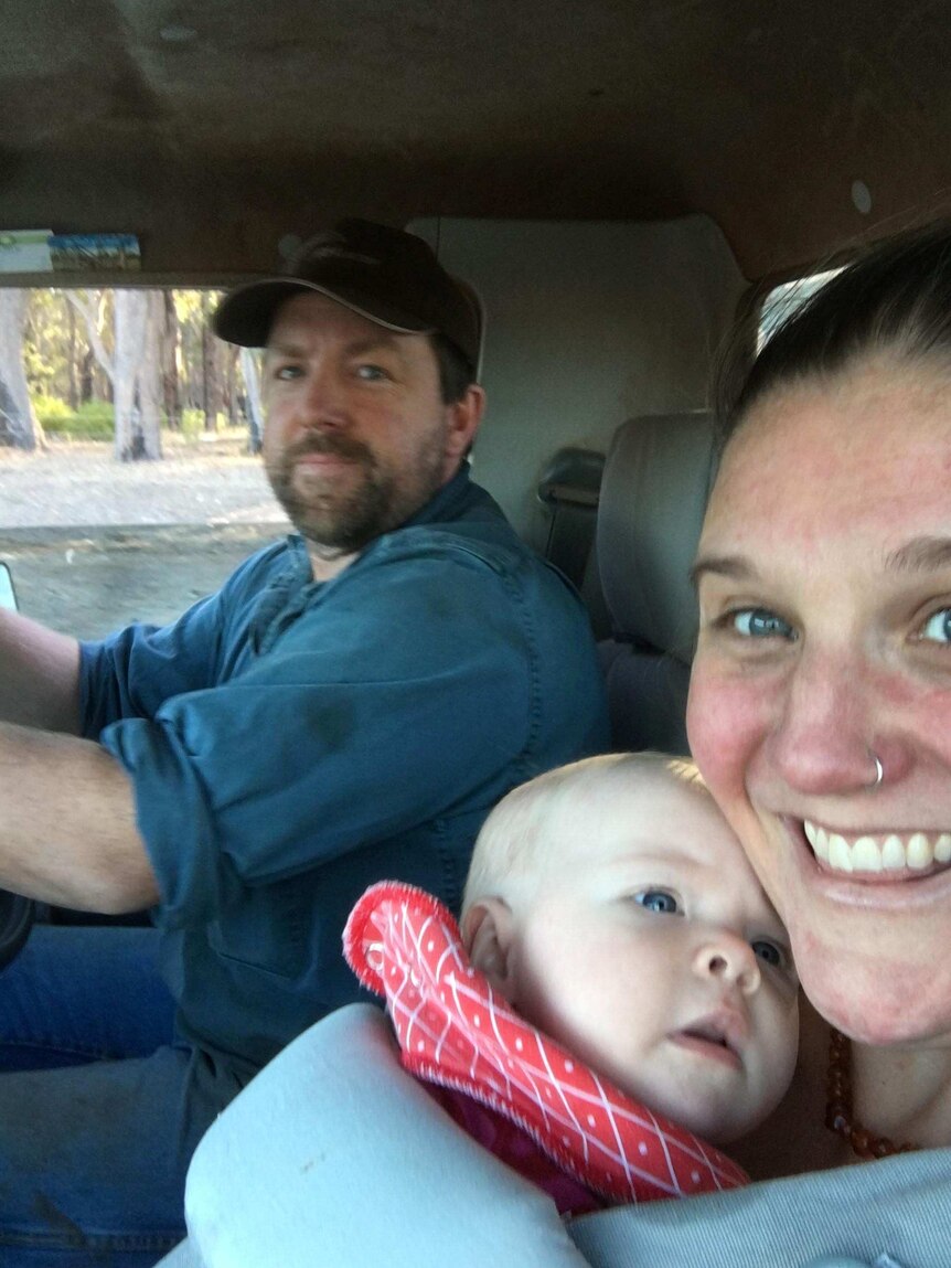 Amy in the cab of a truck with her baby and husband in the driver seat.