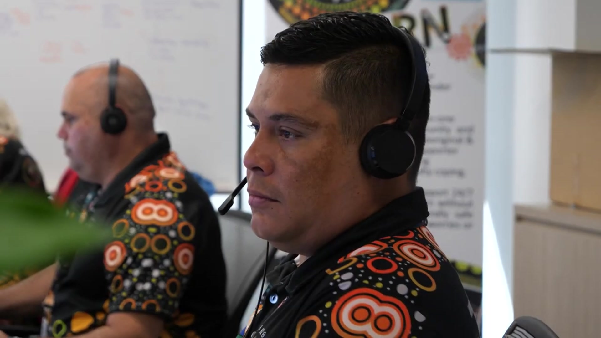 Man in 13YARN call centre wearing a headset. Profile, he is looking away from the camera.