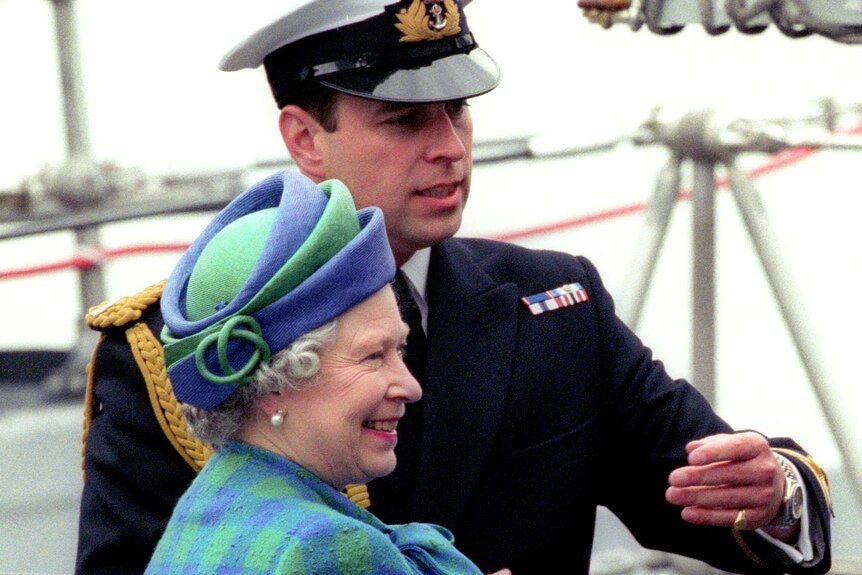 Queen Elizabeth II in blue and green tartan and matching fascinator grins standing next to her son Prince Andrew in Navy uniform