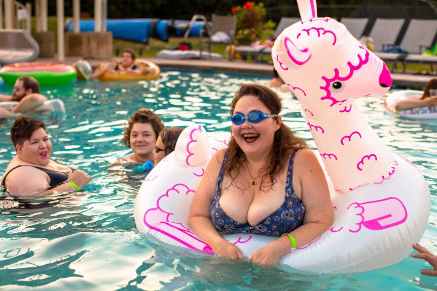 A woman wearing sunglasses floating on a pool toy and smiling