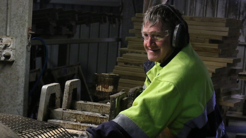 A workers in at a sawmill slides a piece of timber through a saw