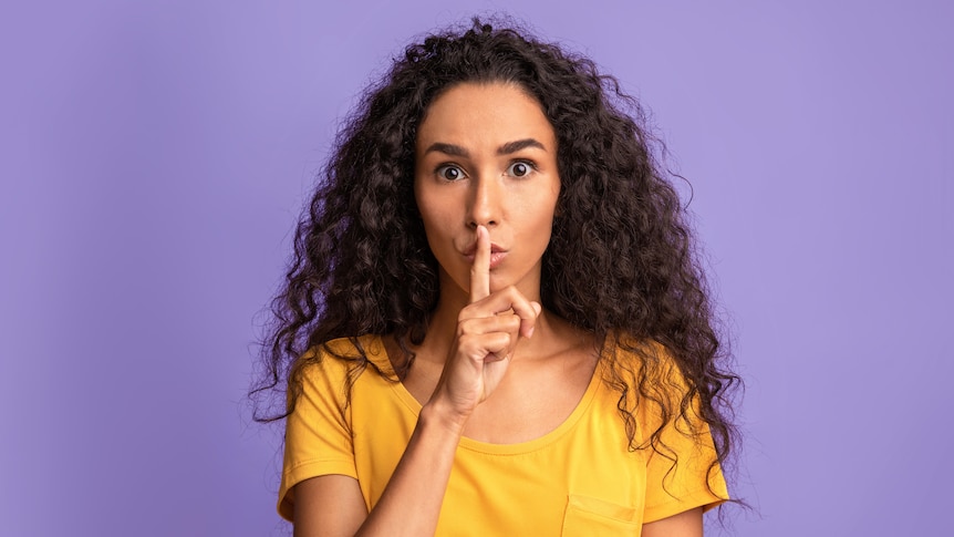 woman holding finger to her mouth making "shhh" gesture against purple background