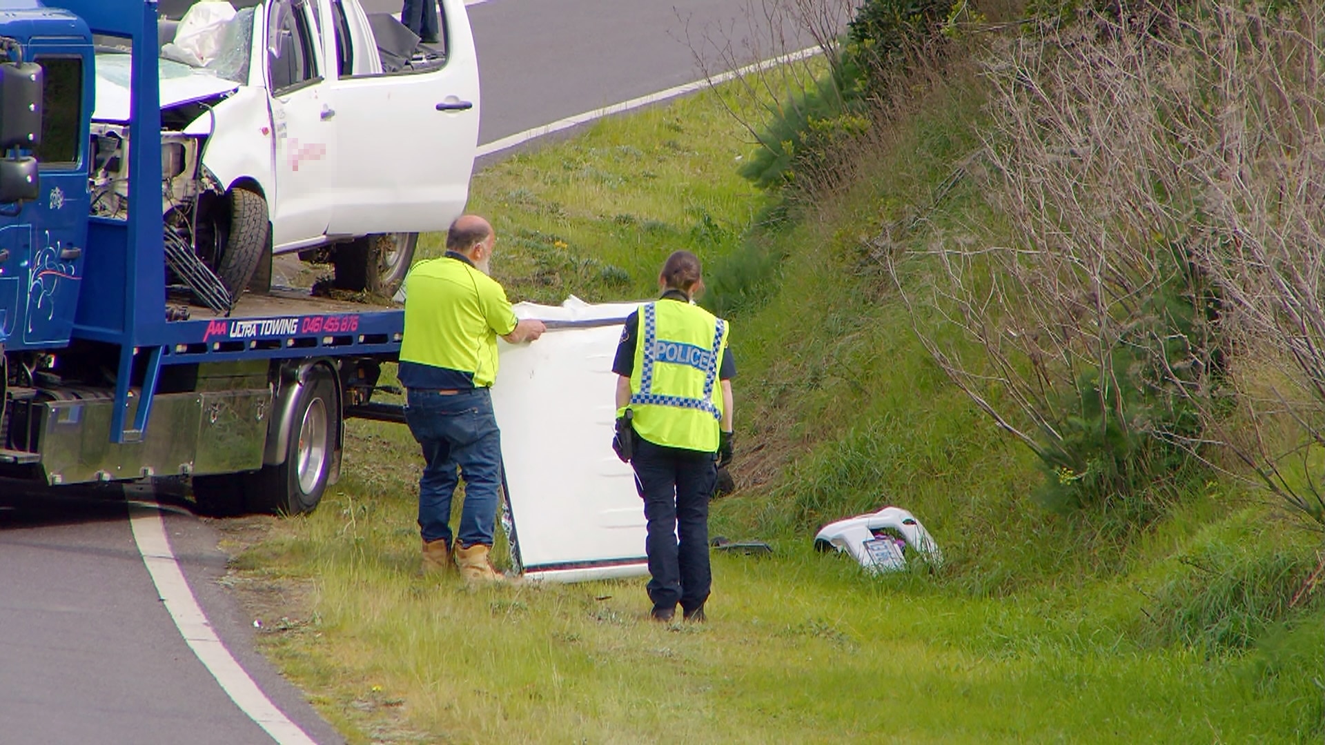 A police officer and tow truck driver stand next to the crash scene