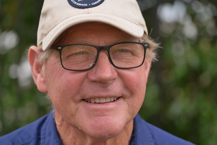 A close up, he is wearing glasses and a cap