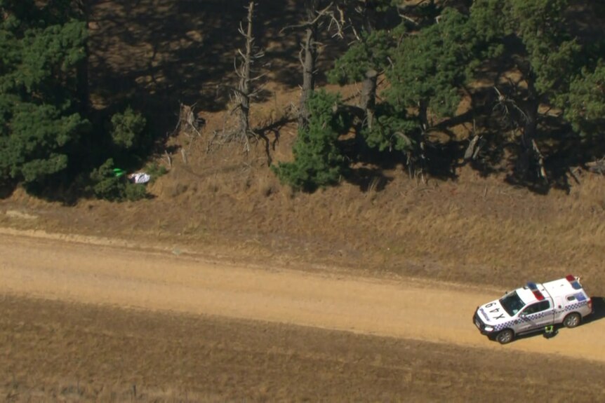Police car on dirt road and hint of bin and cloth to side of road.