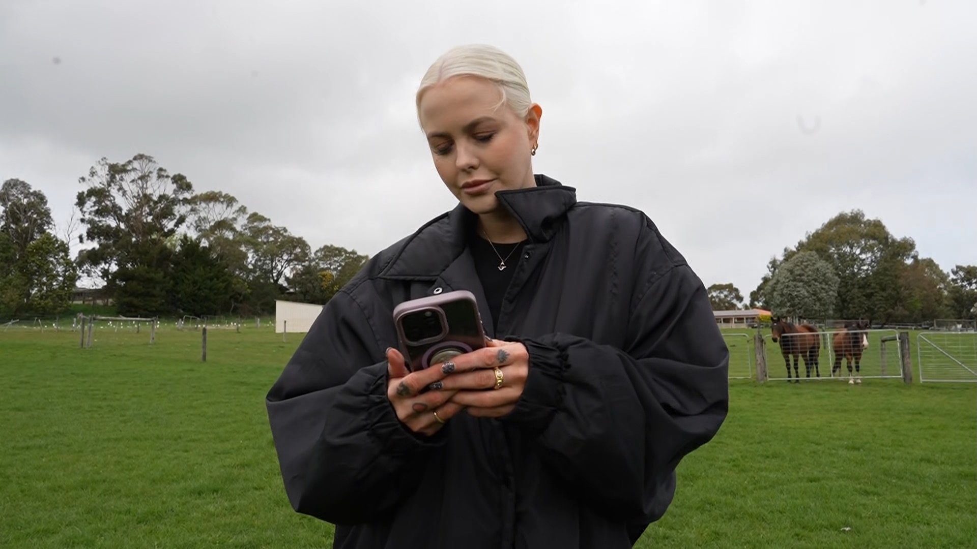 A woman stands outside with a puffer jacket and a mobile phone.