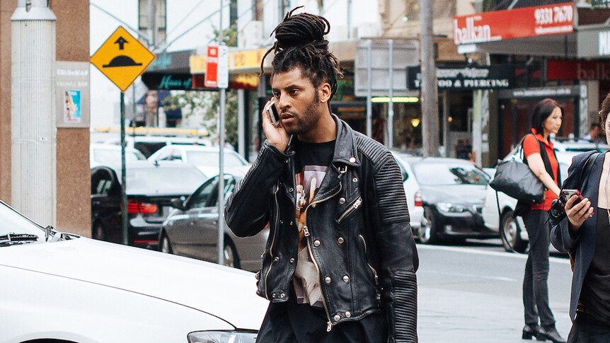 A man wearing a black ribbed leather jacket talks on his phone.