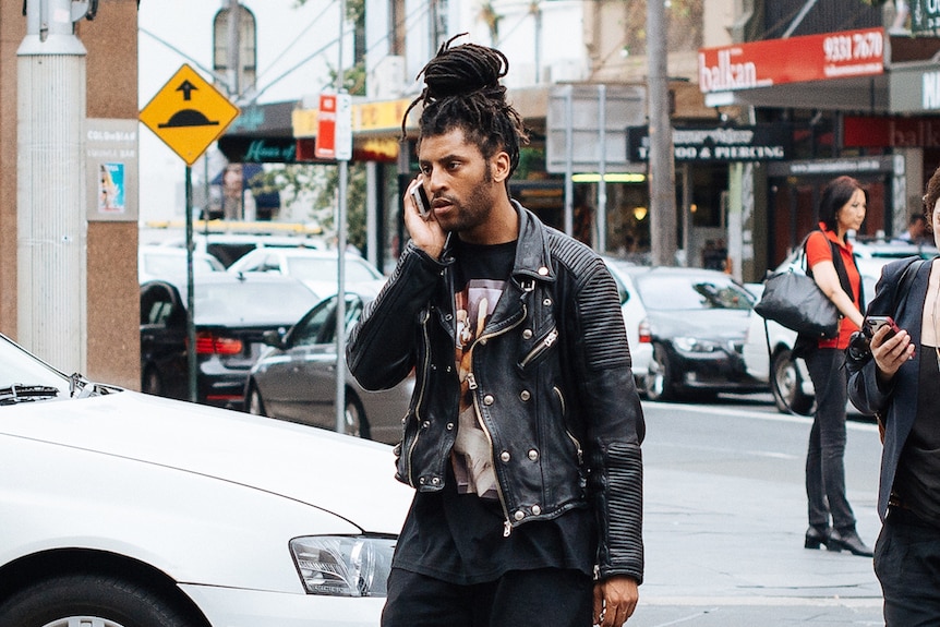 A man wearing a black ribbed leather jacket talks on his phone.