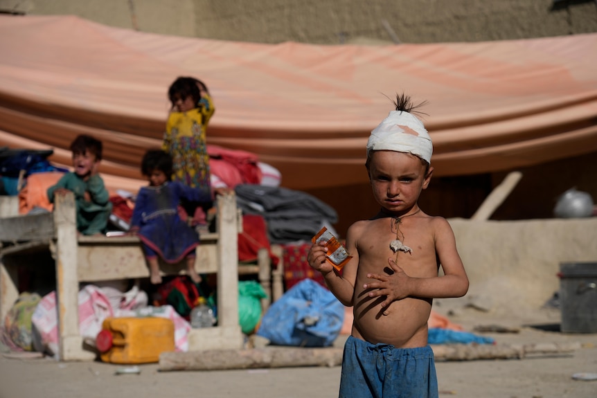A boy stands with his head bandaged at a makeshift shelter