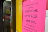 A pink sign with a printed warning that says 'sold out of covid rapid test kits'