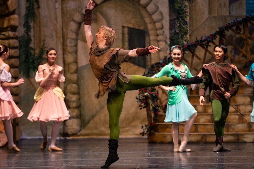 A male ballet dancing in a brown shirt and green tights posing on stage.