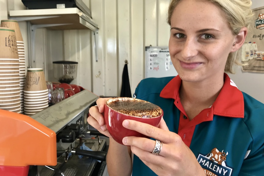 Tiffany Weyman holding up a tilted cup of coffee that shows some of the froth.