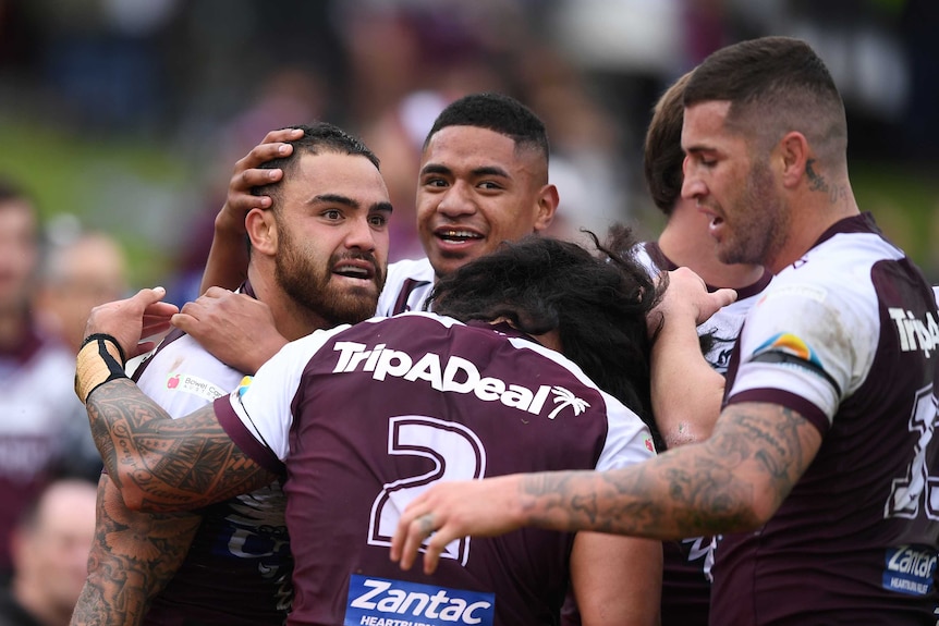 A group of NRL teammates hug and pat each other on the back after a try.