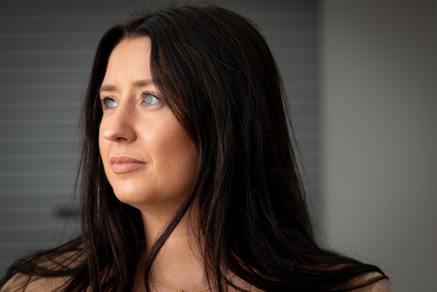 A woman with blue eyes and long dark hair looks off camera with a serious expression