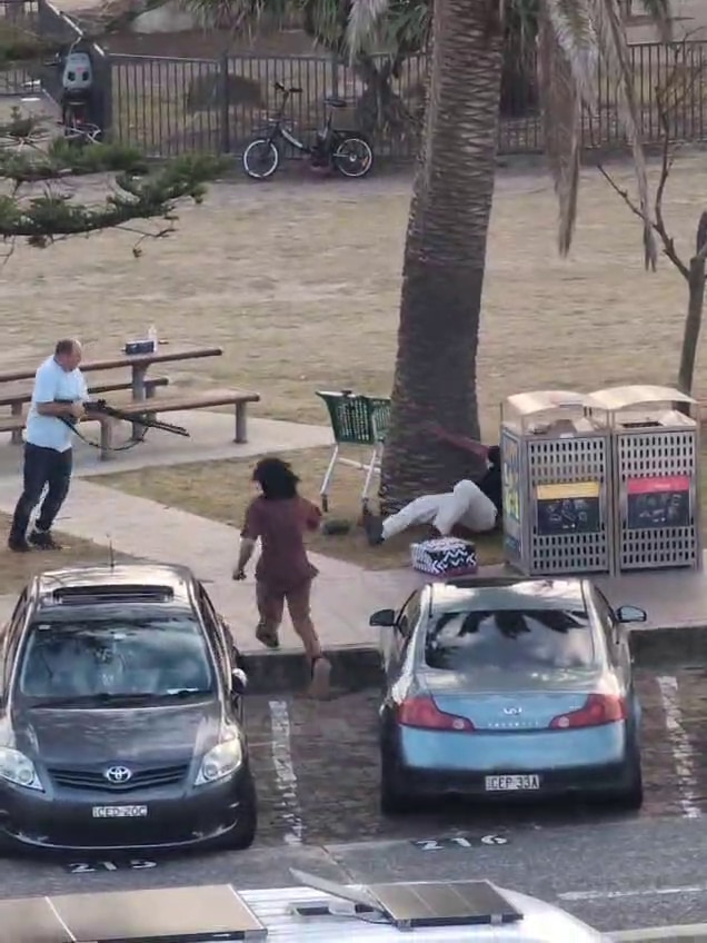 O homem segura uma grande arma que aponta para o homem deitado no chão, com a mão levantada.