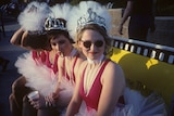 The Go-Go's wearing pearls, tutus and tiaras, sitting on a bench, one member smokes a cigarette