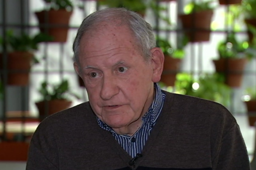 Allen Arthur sitting down wearing a black sweater with green pot plants behind him