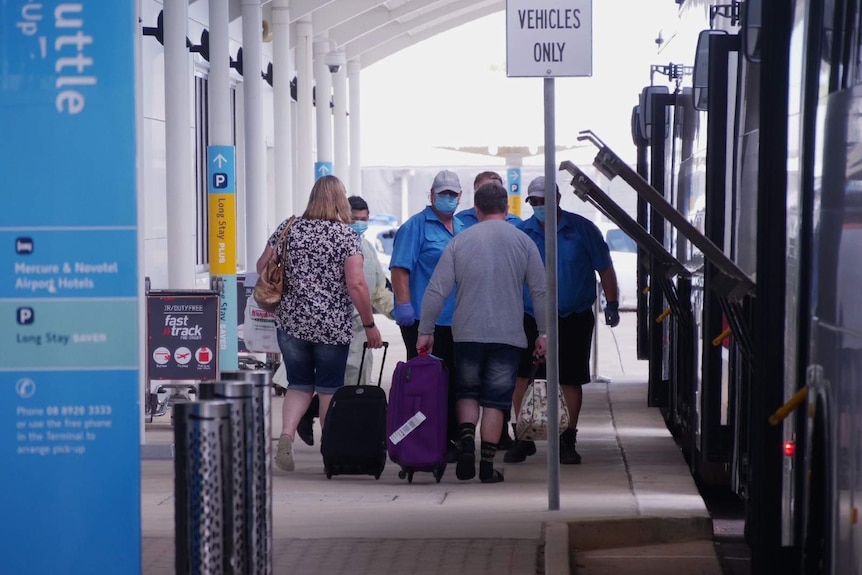 A photo of passengers with luggage boarding a bus outside of the Darwin airport.