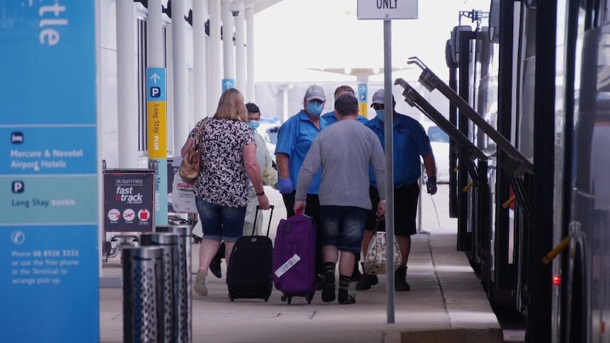 A photo of passengers with luggage boarding a bus outside of the Darwin airport.