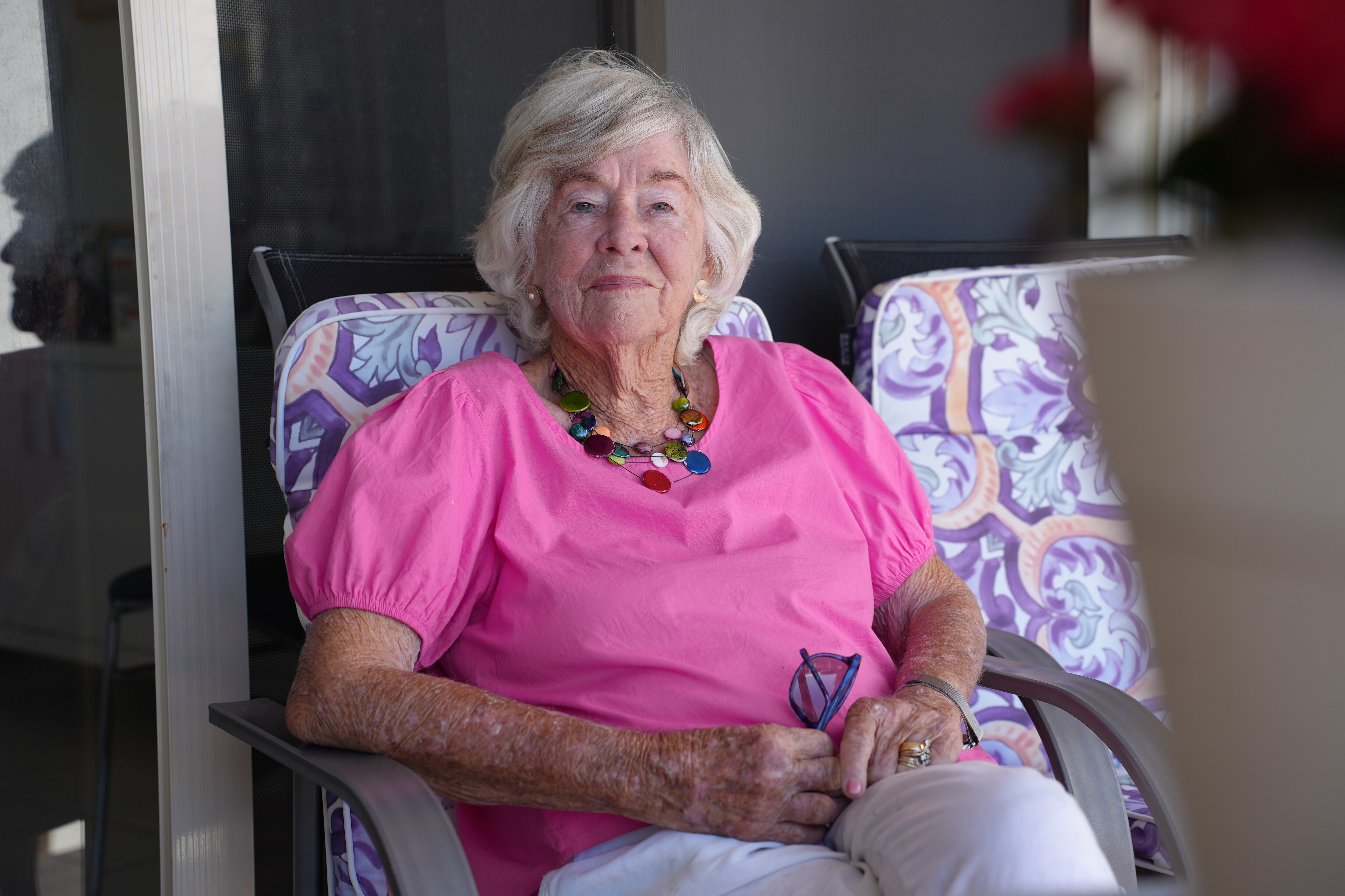 An elderly woman sitting in a chair wearing a bright pink t-shirt