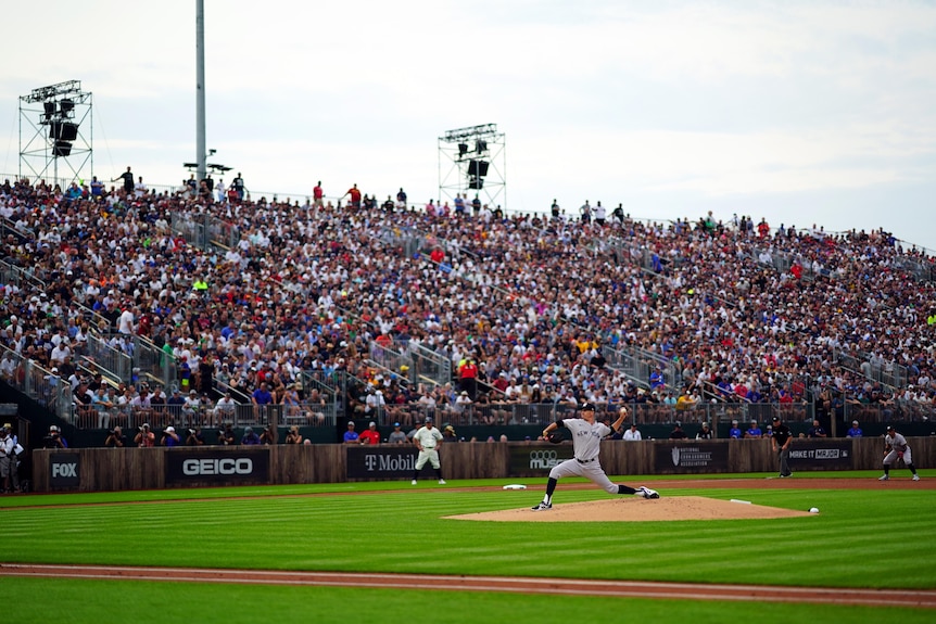 A crowd in the stands watches a baseball player pitch