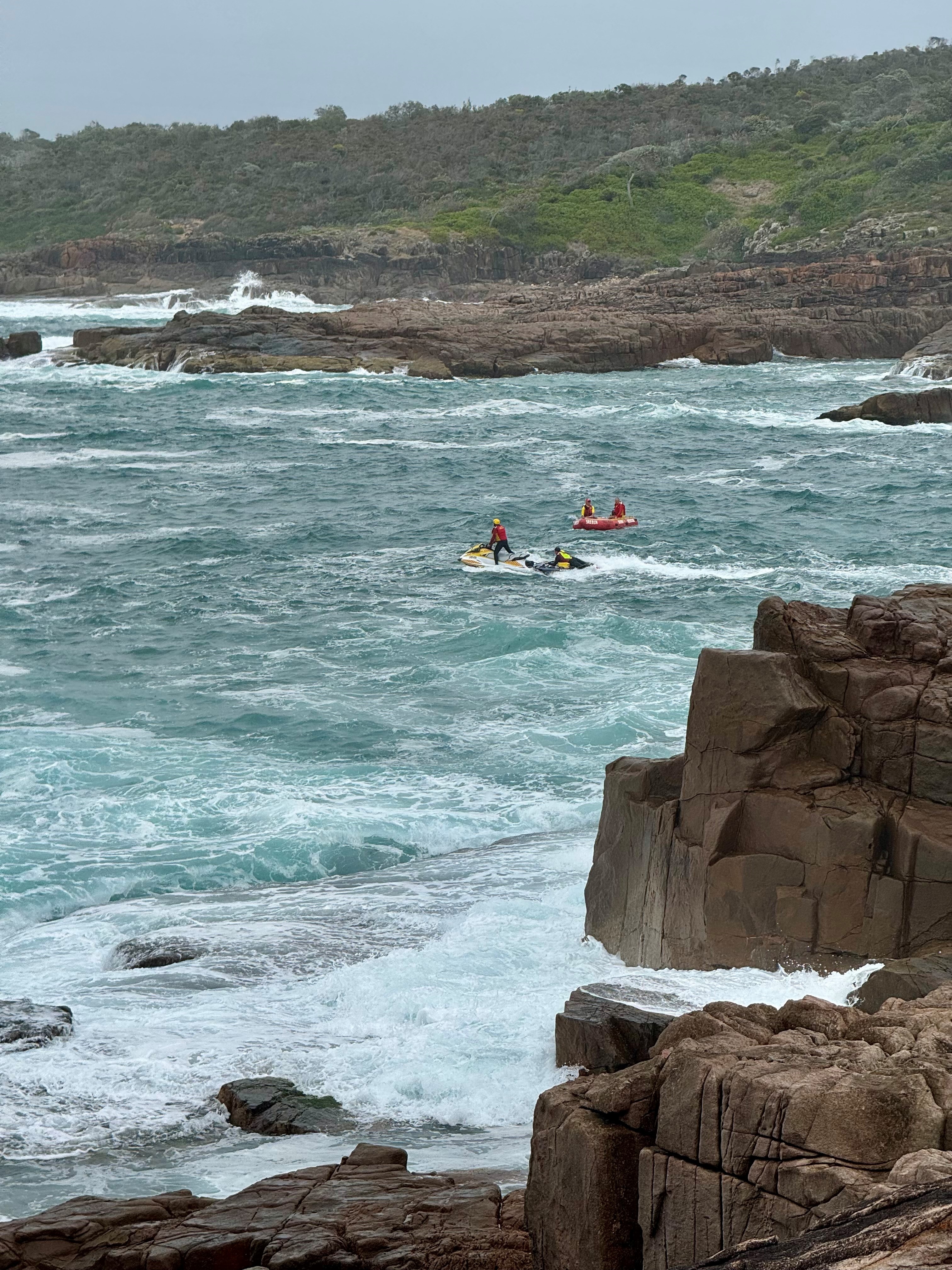 A jet ski in the water near a rocky coastline, searching the water.