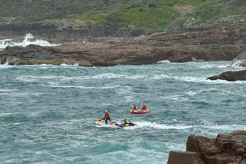 A jet ski in the water near a rocky coastline, searching the water.