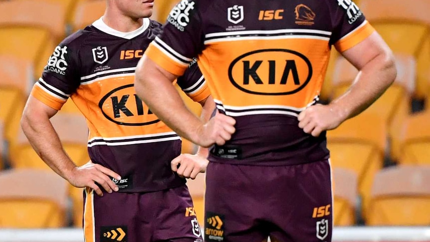 Brisbane Broncos players look up at a scoreboard against a backdrop of empty yellow seats