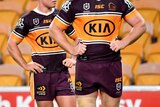 Brisbane Broncos players look up at a scoreboard against a backdrop of empty yellow seats