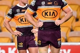 Brisbane Broncos players look up at a scoreboard against a backdrop of empty yellow seats