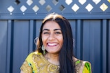 Meera Patel wearing colourful, traditional Indian dress and a bindi, standing in front of gate.