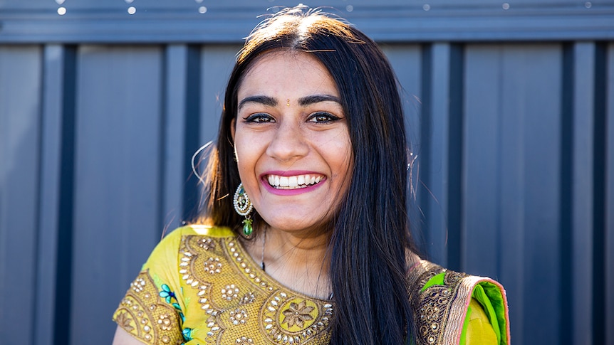 Meera Patel wearing colourful, traditional Indian dress and a bindi, standing in front of gate.