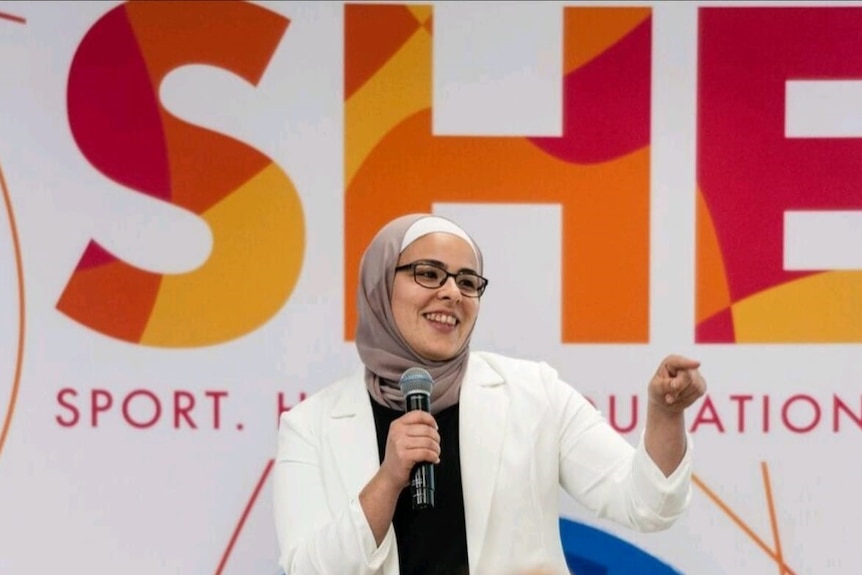 A Muslim woman holds a microphone and talks to a crowd of people. 