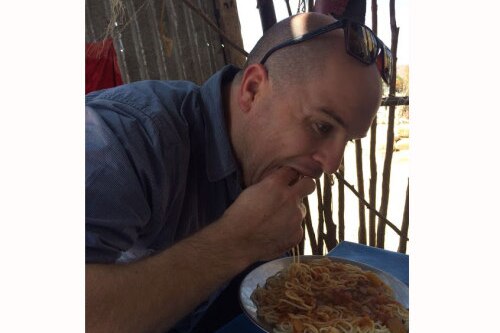 Martin leans over a bowl of spaghetti, eating it with his hands.