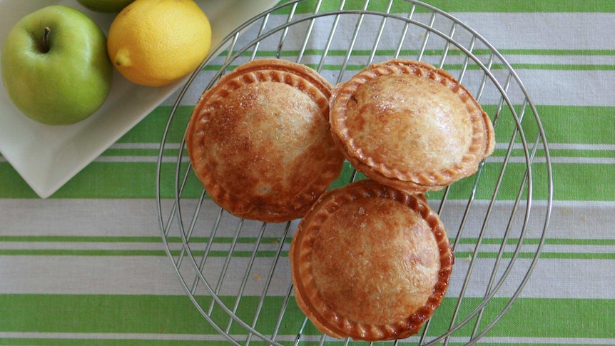 Mini apple pies on a cooling rack with a whole apple and lemon next to the rack