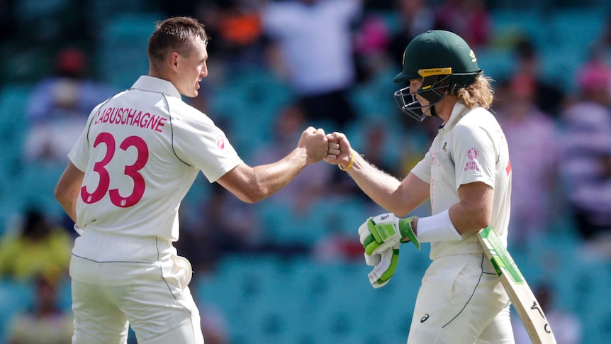 Australia batsmen Marnus Labuschagne (left, without his helmet) and Will Pucovski (right, wearing a helmet) bump fists.