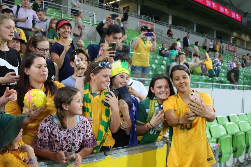 Women's football player Samantha Kerr takes a selfie with fans in the stands.
