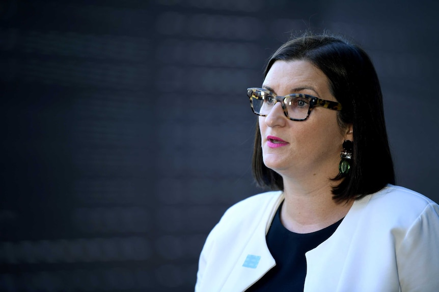 A woman with dark hair and glasses wearing a white blazer.